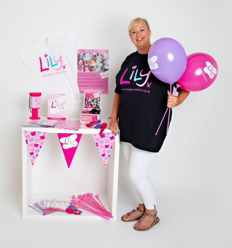 lady in Lily t-shirt next to a stand with balloons, bunting and leaflets